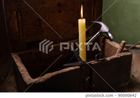 Burning candle in a dark room. The candle is in an old wooden box. Candle and hammer. Burning candle in a dark room. The candle is in an old wooden box. Candle and hammer. 90000642