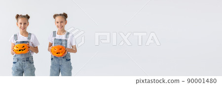 Happy Halloween, banner with copy space holidays and childhood concept - Cute little twins sisters girls with a pumpkins Jack-o'-lantern having fun while spending time indoors 90001480