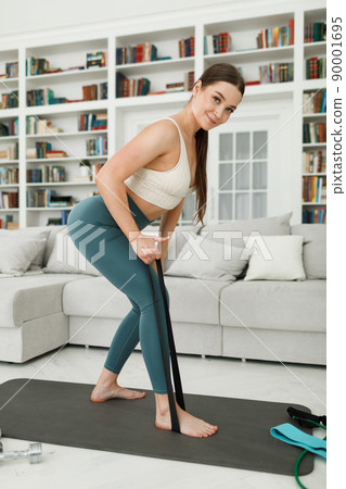 Woman during her fitness workout at home with rubber resistance band Woman during her fitness workout at home with rubber resistance band 90001695