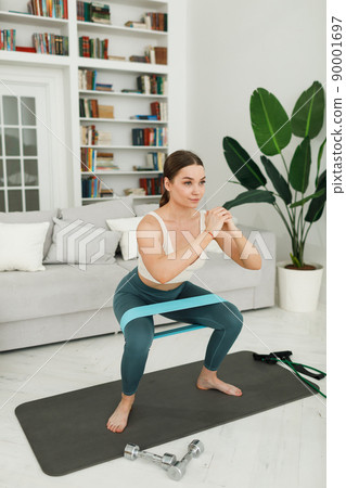 Athletic young woman doing morning exercises squatting alone in the living room, serious girl in 90001697