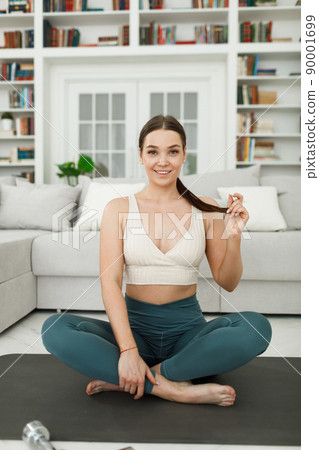 a young woman is preparing to go in for sports, sitting on the floor in a bright living room 90001699