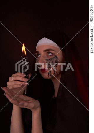Portait of gothic girl looks up and holding wax candle. 90002832