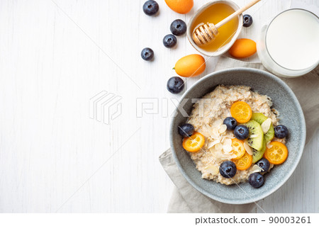 Oatmeal porridge with kumquat, blueberries, kiwi and almond flakes in a bowl. Oatmeal porridge with kumquat, blueberries, kiwi and almond flakes in a bowl. 90003261