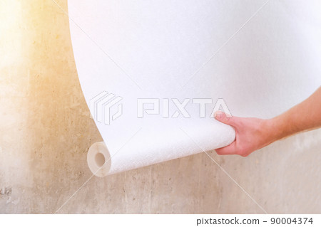 A man rolls out a roll of white wallpaper on the A man rolls out a roll of white wallpaper on the 90004374