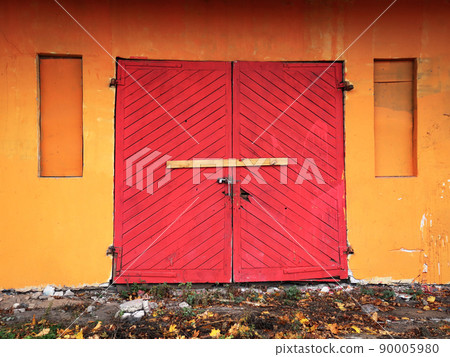 Bright red old wooden garage door double entrance door in orange wall building locked and nailed by a wooden plank Bright red old wooden garage door double entrance door in orange wall building locked and nailed by a wooden plank 90005980