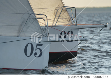 Bowsprits of sailing yachts in sailing regatta at sunset, still water, the clear sky, hot racing Bowsprits of sailing yachts in sailing regatta at sunset, still water, the clear sky, hot racing 90007183