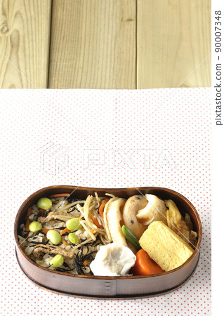 A bird's-eye view of the Makunouchi lunch box containing a lot of side dishes such as hijiki and edamame rice, shumai, omelet, and simmered dishes. 90007348