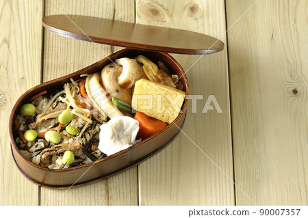 A bird's-eye view of the Makunouchi lunch box containing a lot of side dishes such as hijiki and edamame rice, shumai, omelet, and simmered dishes. 90007357