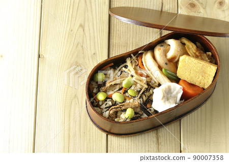 A bird's-eye view of the Makunouchi lunch box containing a lot of side dishes such as hijiki and edamame rice, shumai, omelet, and simmered dishes. 90007358