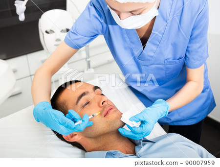 Man receiving face injections at beauty clinic Man receiving face injections at beauty clinic 90007959