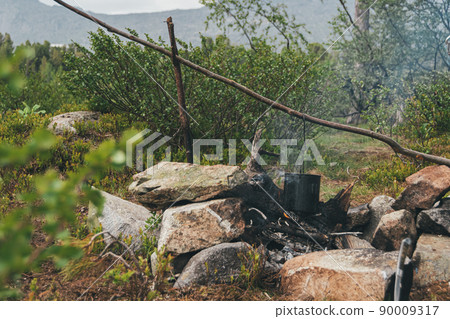 Tourist pot hangs over campfire. Survival in wild for cooking. Organization of hearth of stones for heating. Tourist pot hangs over campfire. Survival in wild for cooking. Organization of hearth of stones for heating. 90009317