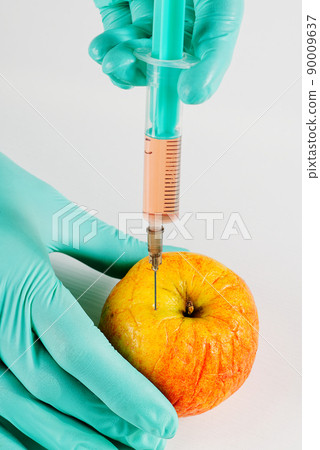 A hand in a medical glove inserts a syringe into apple. Harmful food additives. GMOs Concept A hand in a medical glove inserts a syringe into apple. Harmful food additives. GMOs Concept 90009637
