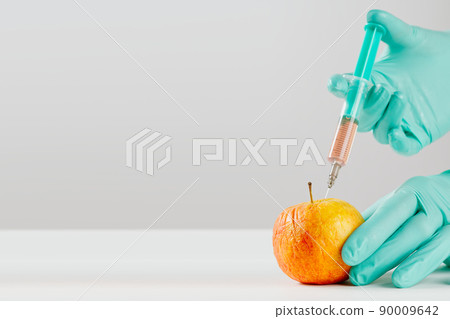 A hand in a medical glove inserts a syringe into apple. Harmful food additives. GMOs Concept A hand in a medical glove inserts a syringe into apple. Harmful food additives. GMOs Concept 90009642