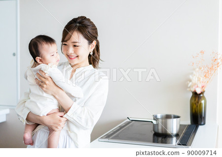 A young woman doing household chores while holding a baby 90009714