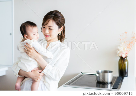 A young woman doing household chores while holding a baby A young woman doing household chores while holding a baby 90009715