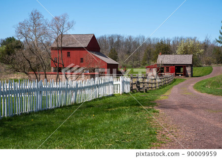 Dirt road with picket fence and a colonial American red barn and log cabin 90009959