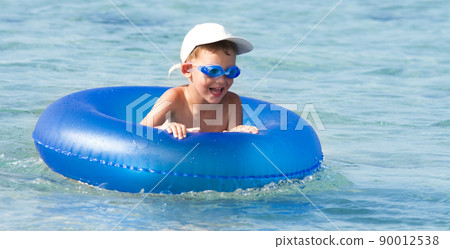 Happy boy with blond hair smiling sitting in swimming pool 90012538