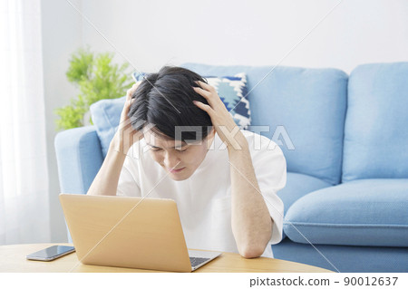 A man holding his head in front of a laptop in the living room A man holding his head in front of a laptop in the living room 90012637