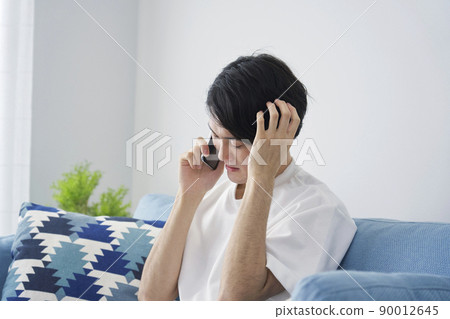 一個男人在客廳裡用智能手機抱著頭 90012645