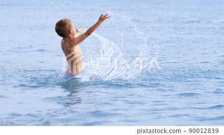 Happy boy with blond hair smiling sitting in swimming pool 90012839