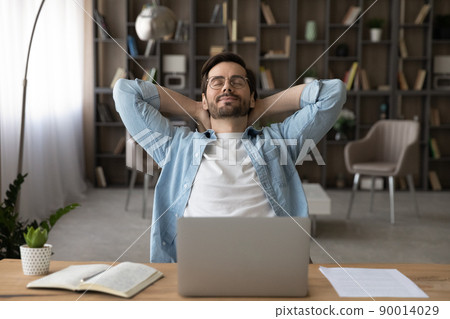 Happy young guy freelancer relax at work desk close eyes 90014029