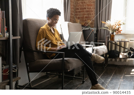 Young African woman sit on armchair using modern laptop Young African woman sit on armchair using modern laptop 90014435