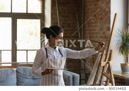 Indian woman painter painting on canvas in modern workshop 90014488