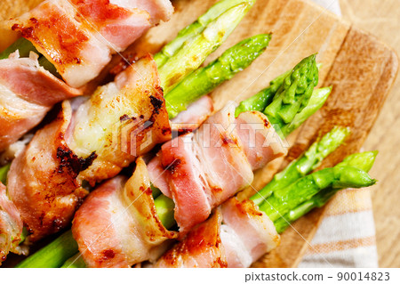 Bacon wrapped asparagus on wooden plate. 90014823