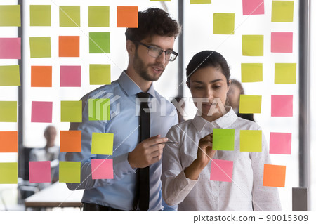 Multi ethnic colleagues discuss creative ideas on sticky post-it notes 90015309