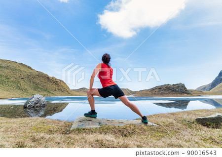 A young woman practices gymnastics in front of an alpine pond A young woman practices gymnastics in front of an alpine pond 90016543