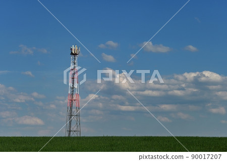 Telecommunication Tower - Transmitter for gsm signal of mobile phones in the field. In the background blue sky with clouds. Concept for modern technology and industry. Telecommunication Tower - Transmitter for gsm signal of mobile phones in the field. In the background blue sky with clouds. Concept for modern technology and industry. 90017207