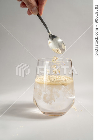 Woman pours collagen powder or protein in a glass of water on a beige background. A healthy and anti aging supplement. Copy space 90018383