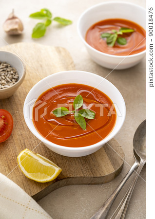 Tomato soup with fresh basil in white bowls. Served with sunflower seeds. Bright background. Top view, copy space. 90018476