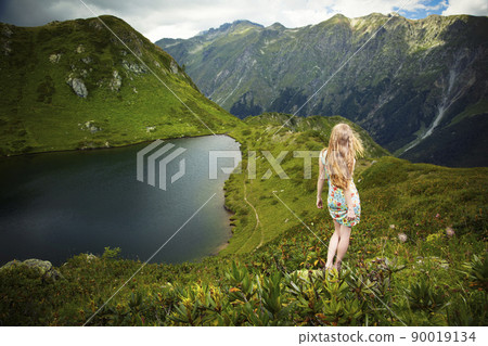 Beautiful young woman with red hair standing on a rock and looking at the lake Beautiful young woman with red hair standing on a rock and looking at the lake 90019134