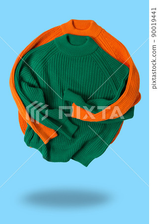 two wool knitted sweaters, green and orange, folded as if hugging, levitating, on a cyan background, concept two wool knitted sweaters, green and orange, folded as if hugging, levitating, on a cyan background, concept 90019441