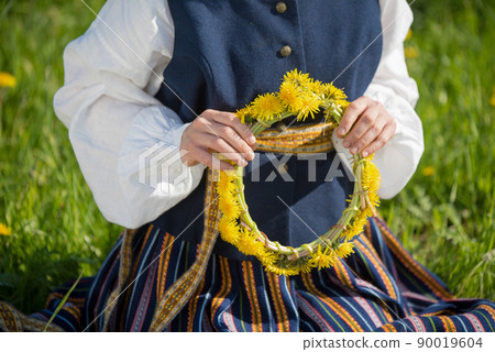 Young woman in national clothes wearing yellow dandelion wreath in spring field. Springtime Young woman in national clothes wearing yellow dandelion wreath in spring field. Springtime 90019604