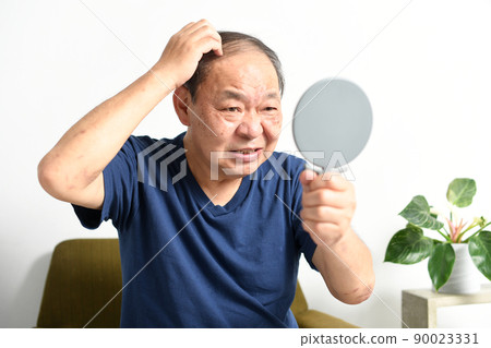 Middle-aged and older men suffering from thinning hair while looking in the mirror 90023331