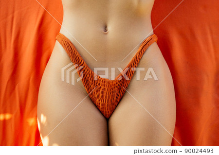Close-up beautiful luxury slim girl in a coral orange bikini lying on a lounger massage table on the beach ocean. Sexy tanned girl body, flat stomach, perfect figure sunscreen spf. Close-up beautiful luxury slim girl in a coral orange bikini lying on a lounger massage table on the beach ocean. Sexy tanned girl body, flat stomach, perfect figure sunscreen spf. 90024493