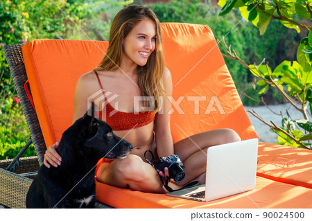remote work on the beach freelancing girl in a coral bathing suit sitting in a lounge chair and the beach with a laptop.business lady online purchase black Friday sale on vacation in tropical country 90024500