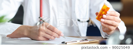 A woman doctor is holding a medicine makes notes in the documents A woman doctor is holding a medicine makes notes in the documents 90025049