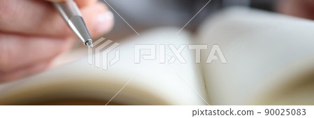 Woman's hand holding a pen near notepad, close-up 90025083