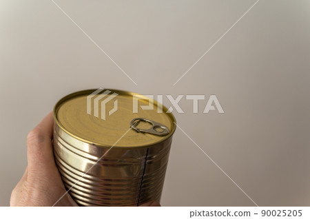 Close-up of a man's hand holding a canned food. Canned food in a metal cylindrical container. Closed Tin can with ready-to-eat food. Selective focus. 90025205
