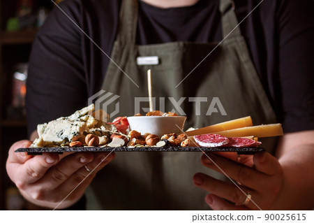 Waitress holding black stone board with delicacies. Waitress holding black stone board with delicacies. 90025615