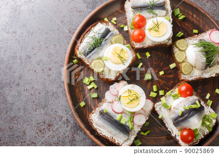 Rye bread toasts with butter, sprat fillet, eggs, various vegetables close-up in a plate. Horizontal top view 90025869