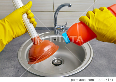 Hands in yellow rubber gloves hold a plunger and a pipe cleaner 90026174