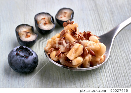 Spoon with cereal oatmeal and flax seeds surrounded by blueberries Spoon with cereal oatmeal and flax seeds surrounded by blueberries 90027456