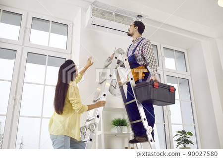 Repairman repairs air conditioner and cleans air filter on indoor unit at client's home. 90027580