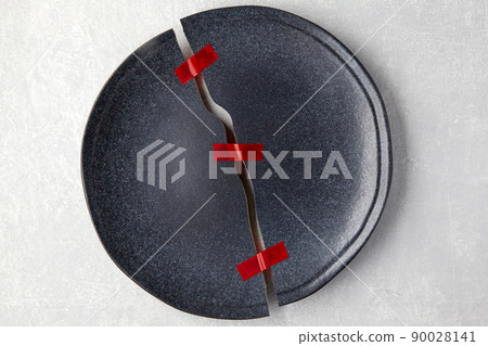 Broken plate is taped together on a light gray concrete table 90028141