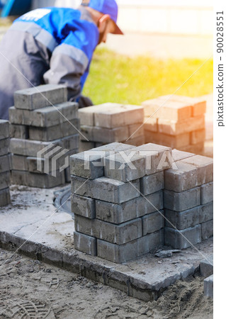 Bricklayer in work clothes sits on sidewalk and lays out paving slabs. Sight of working man in open 90028551