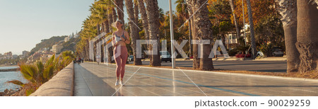 Sporty happy female actively running by the waterfront Sporty happy female actively running by the waterfront 90029259